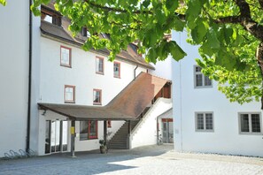 A building with a white facade, red-framed windows, a staircase, and a covered entrance area. - Kloster Heiligkreuztal Tagungshaus (Altheim)