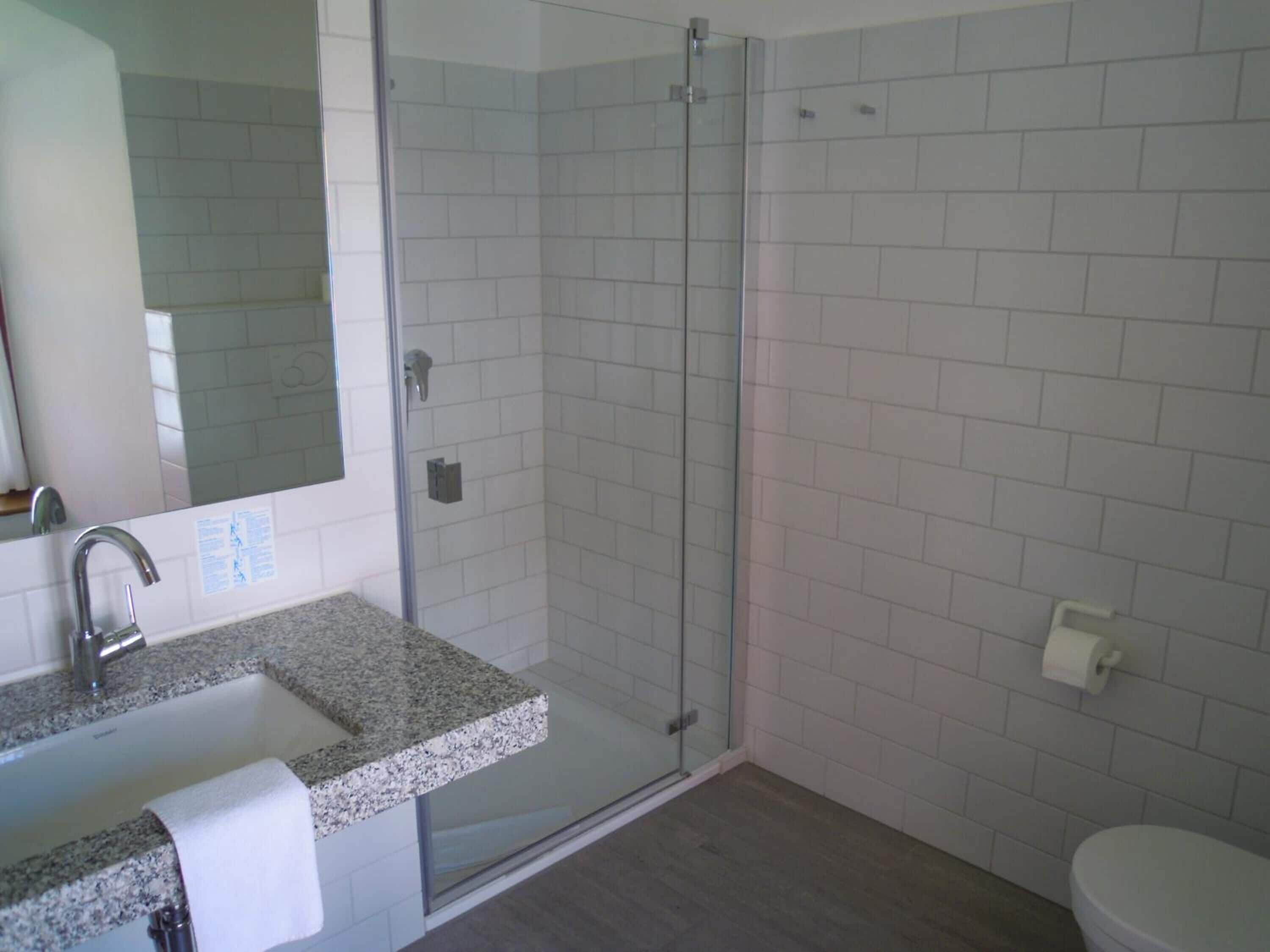 Ein Badezimmer mit Marmorwaschtisch, einer Duschkabine aus Glas und einer weißen Toilette.