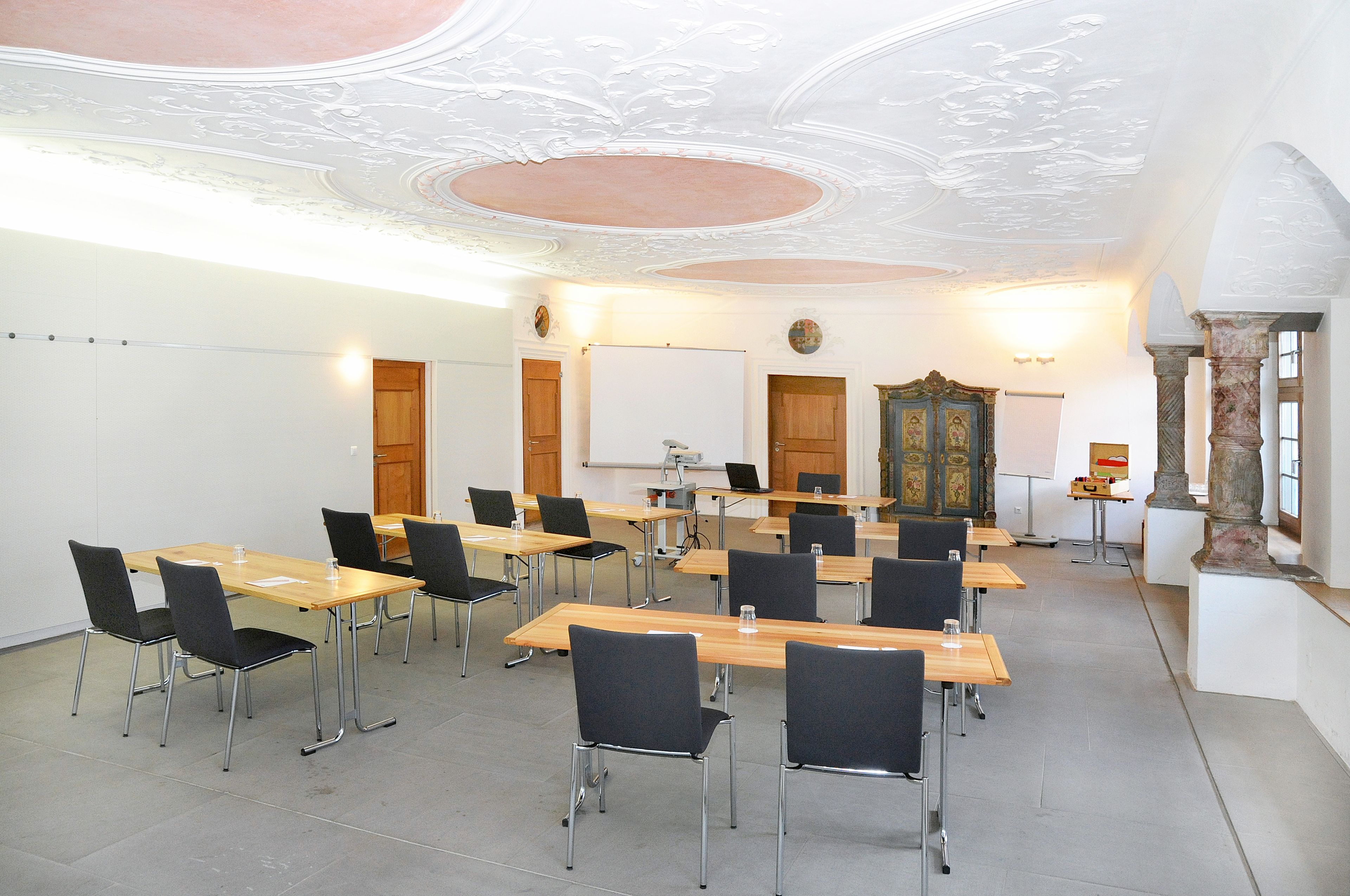 A conference room with tables and chairs, a whiteboard, and a decorative cabinet.