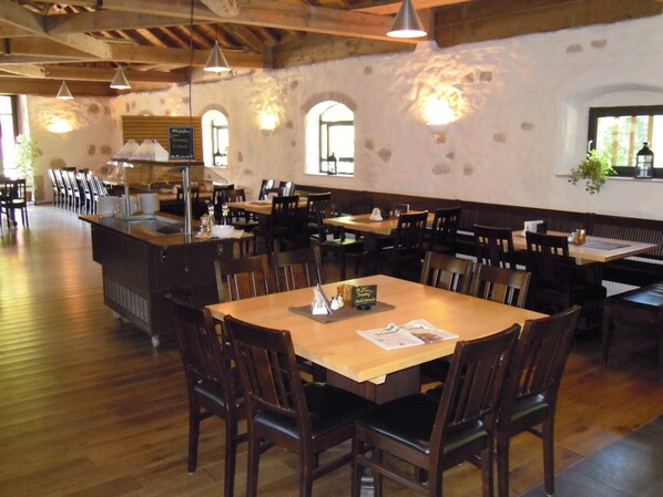 A restaurant interior with wooden tables and chairs, stone walls, and hanging pendant lights. - Kloster Heiligkreuztal Tagungshaus (Altheim)