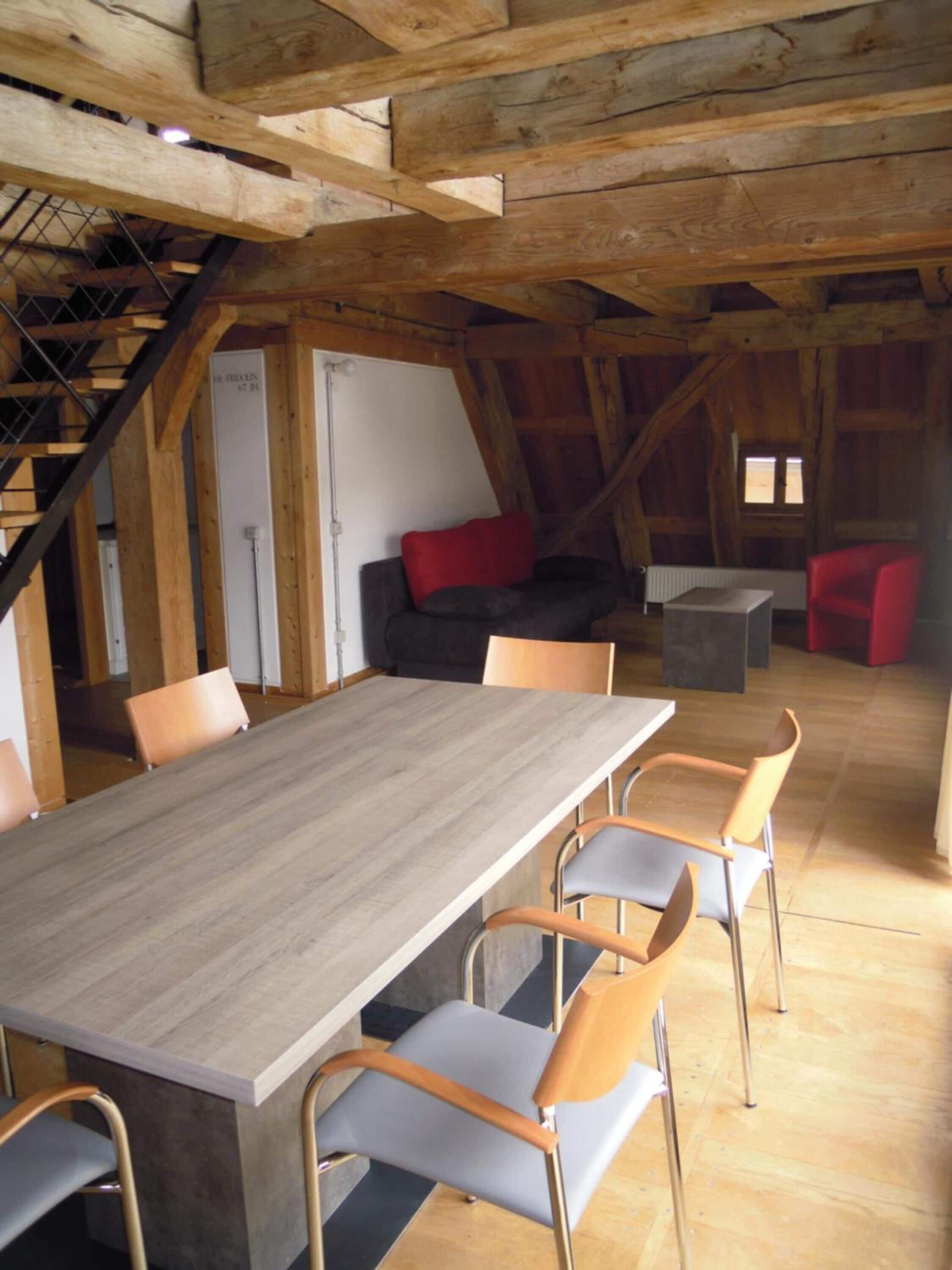Un interior rústico de madera con una larga mesa de comedor, varias sillas, un sofá y una escalera.
