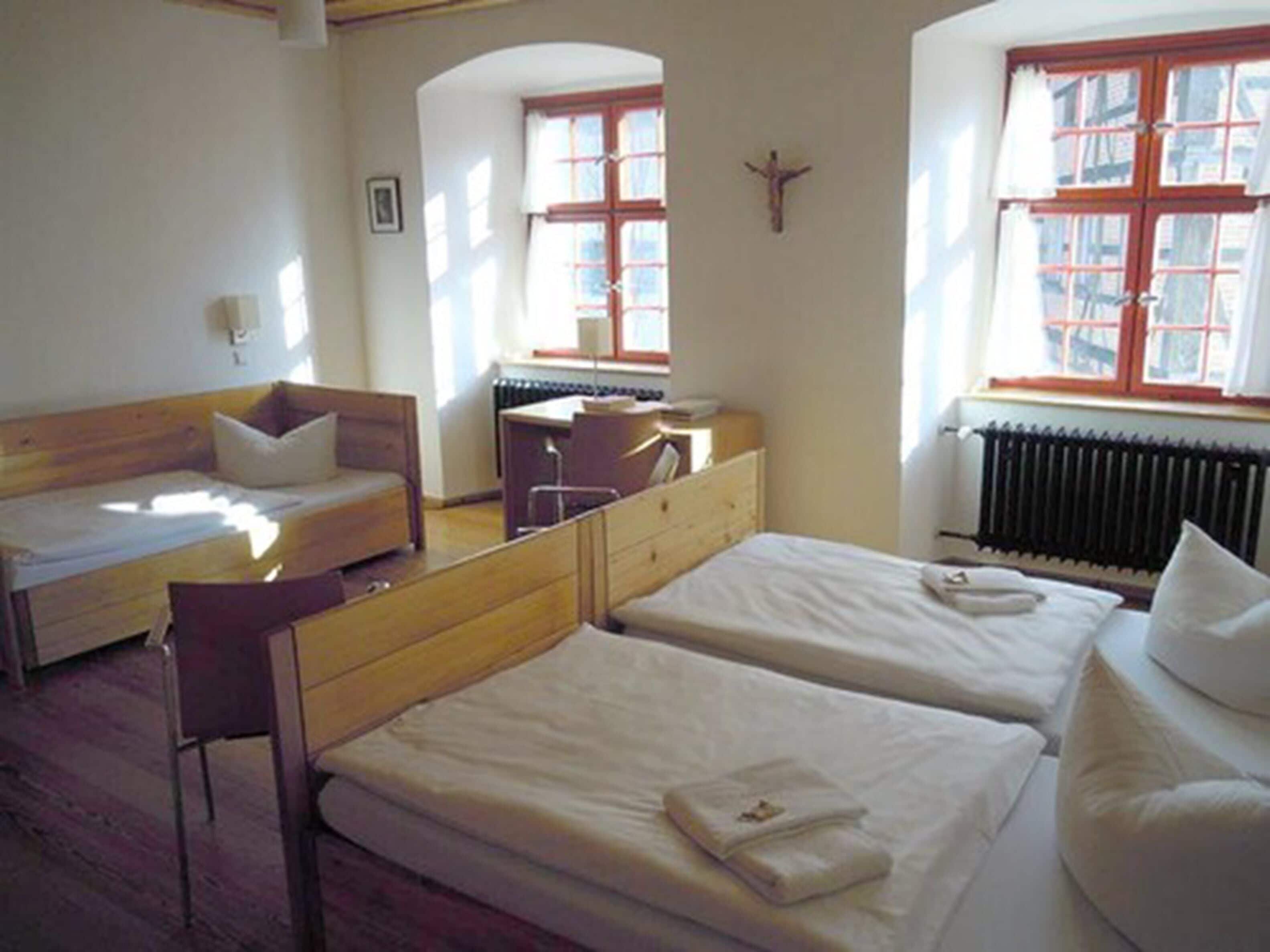 A room with two beds, a desk, a chair, and a radiator.