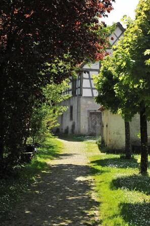 Ein schmaler Pflasterweg führt zu einem traditionellen Gebäude mit freiliegenden Holzbalken und einer Tür mit geometrischem Muster.