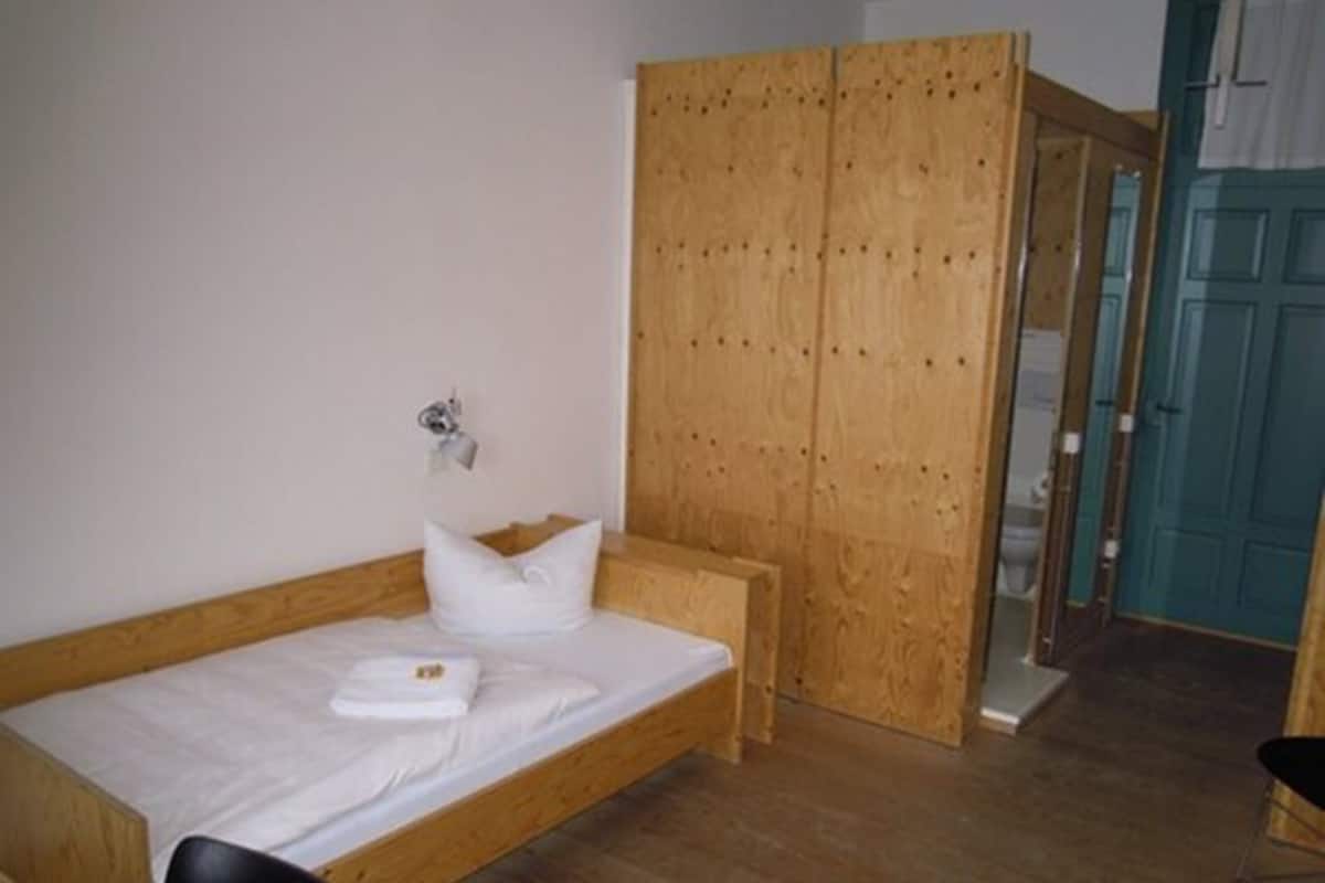 A small, single-bed room with a wooden wardrobe and a bench.