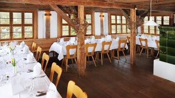 Een restaurant met houten balken, witte tafels en stoelen.