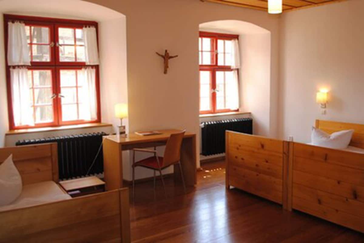 A room with a wooden bed, a desk with a chair, and a radiator.