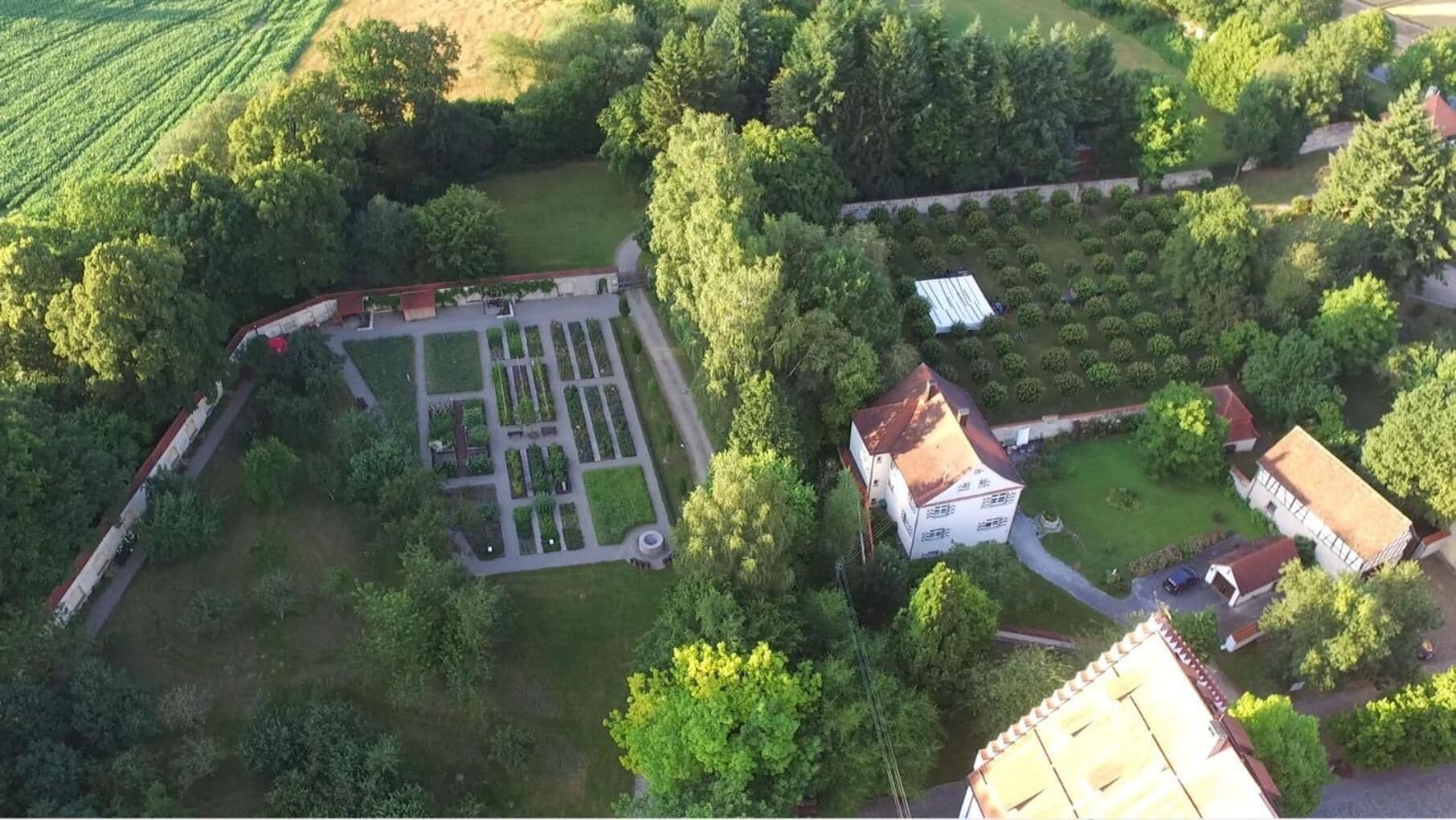 An aerial view of a property with a large garden, a central courtyard, and several buildings with red-tiled roofs.