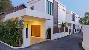 A modern two-story residential building with a flat roof, large windows, and a gated entrance. - Exquisite Thai Balinese Pool Villa Mika (Rawai)