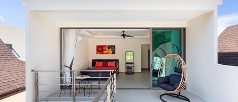 Um interior moderno com varanda, uma cadeira suspensa e uma cama com roupa de cama vermelha.