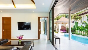 A modern living room with a flat-screen TV, a sofa, and a coffee table with a vase of flowers. - Exquisite Thai Balinese Pool Villa Mika (Rawai)