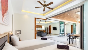 A modern hotel room with a large bed, a desk, a chair, a ceiling fan, and a view of the kitchen and dining area. - Exquisite Thai Balinese Pool Villa Mika (Rawai)