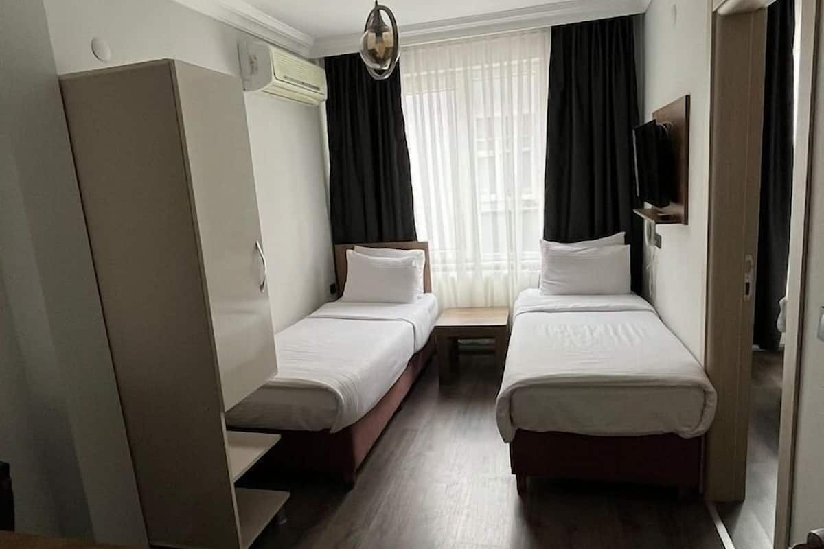 Une chambre d’hôtel avec deux lits simples, un bureau en bois, un téléviseur fixé au mur et un luminaire au plafond.
