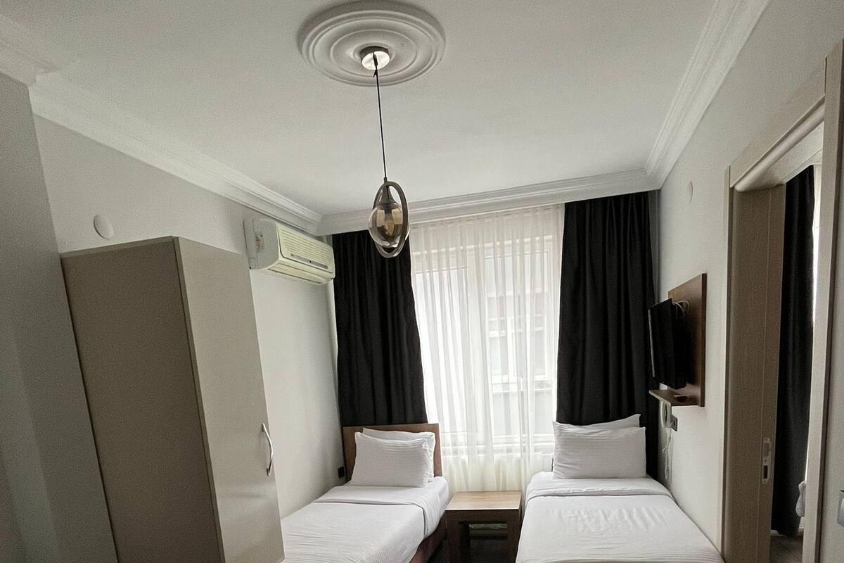 Une chambre d’hôtel avec deux lits simples, un bureau, une chaise, une télévision et une fenêtre avec des rideaux.