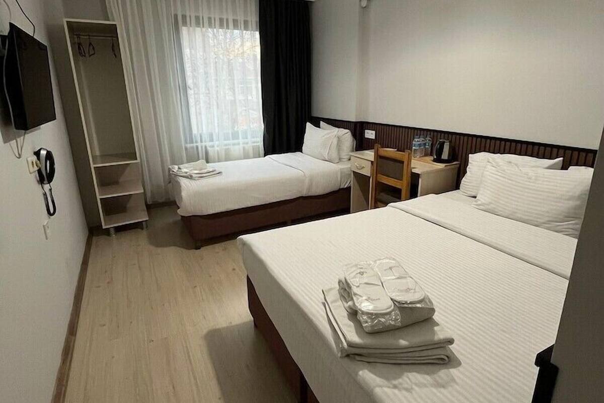 Une chambre d’hôtel avec deux lits, un bureau, une chaise, une télévision, une armoire et une fenêtre avec des rideaux.
