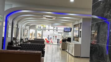 Un hall de hotel con recepción, zona de estar y vistas a la calle.