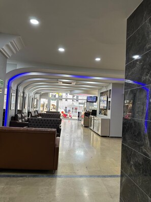 A hotel lobby with a reception desk, seating area, and a view of the street outside.