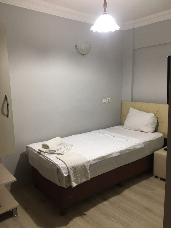 A single bed with a headboard, a bedside table, and a wall-mounted light fixture.