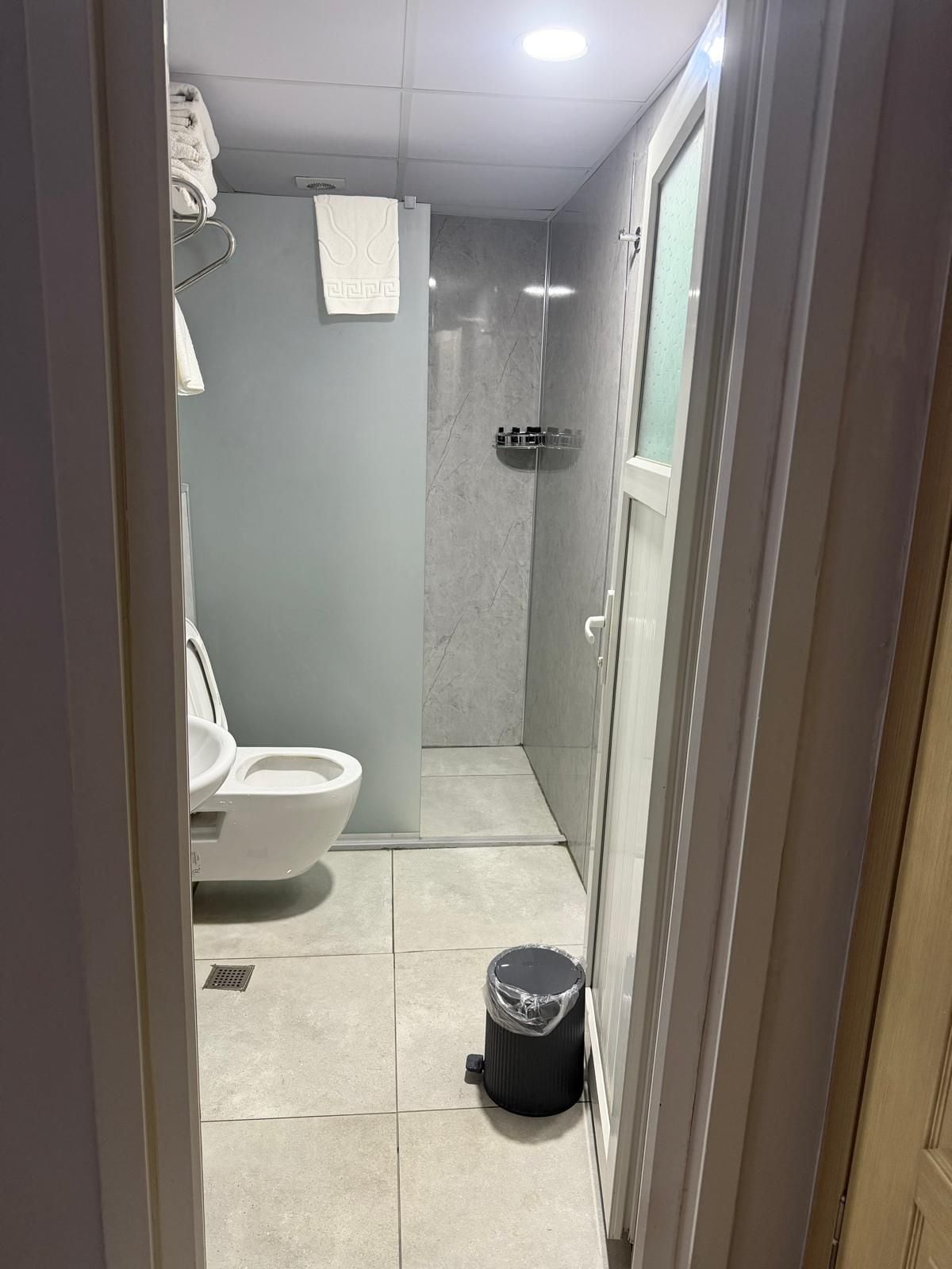 Un baño con inodoro, cabina de ducha y cubo de basura.