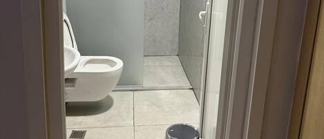 Un baño con inodoro, cabina de ducha y cubo de basura.