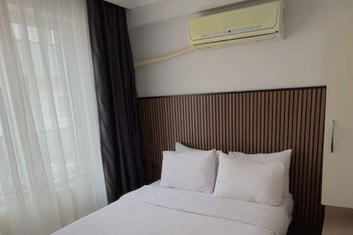 Une chambre d’hôtel moderne avec un grand lit, un luminaire au plafond, un appareil de climatisation et une tête de lit en bois.