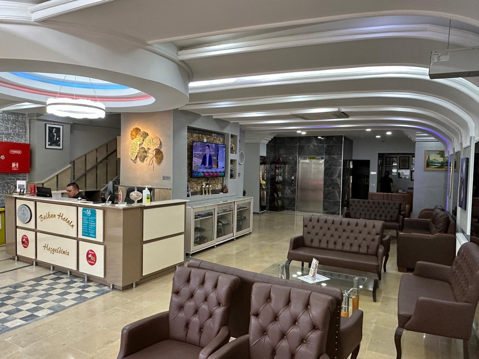 A hotel lobby with a reception desk, seating area, and a television screen.