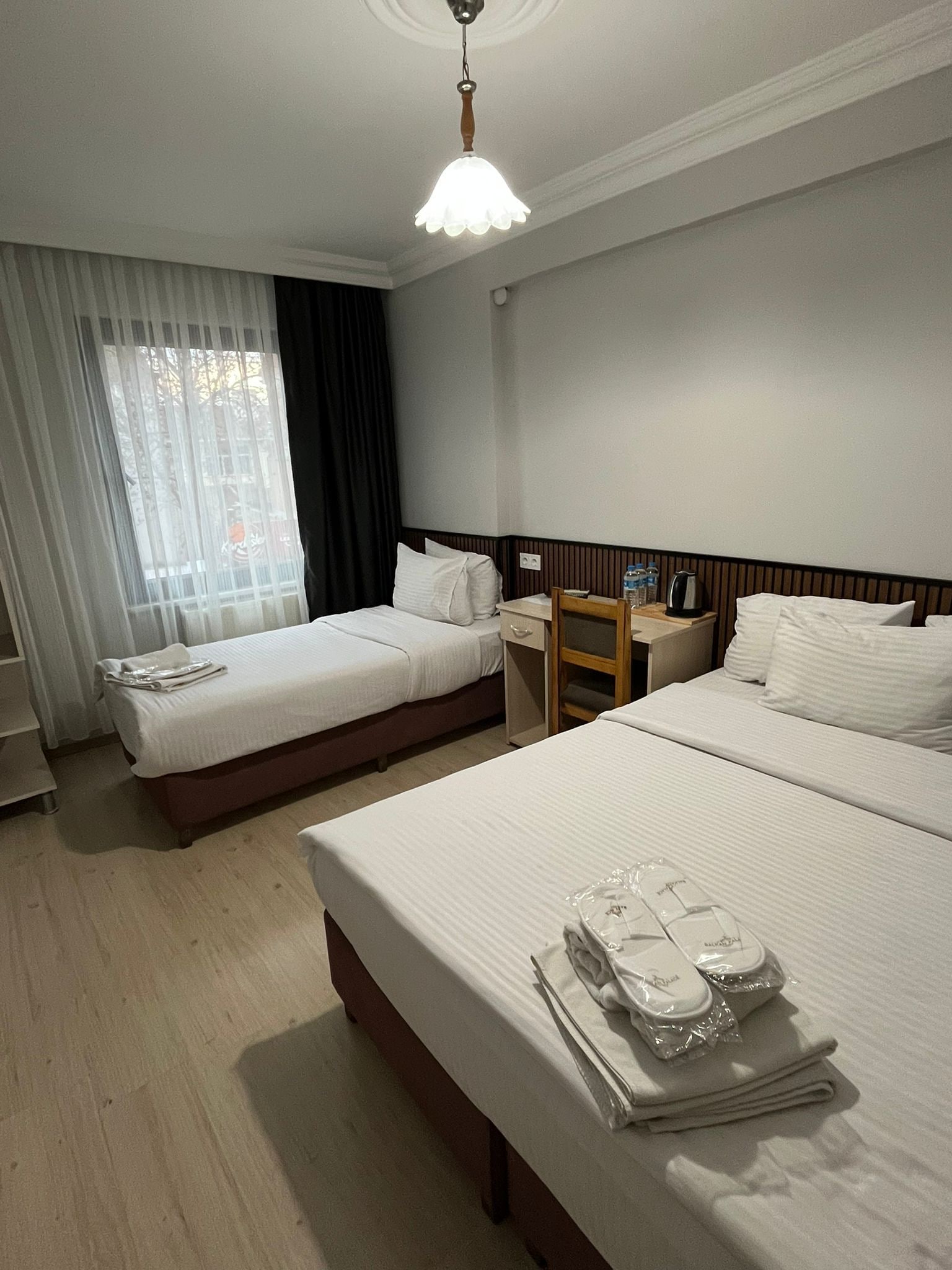 Quarto de hotel com duas camas, uma escrivaninha, uma cadeira e uma janela com cortinas.