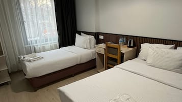 Quarto de hotel com duas camas, uma escrivaninha, uma cadeira e uma janela com cortinas.