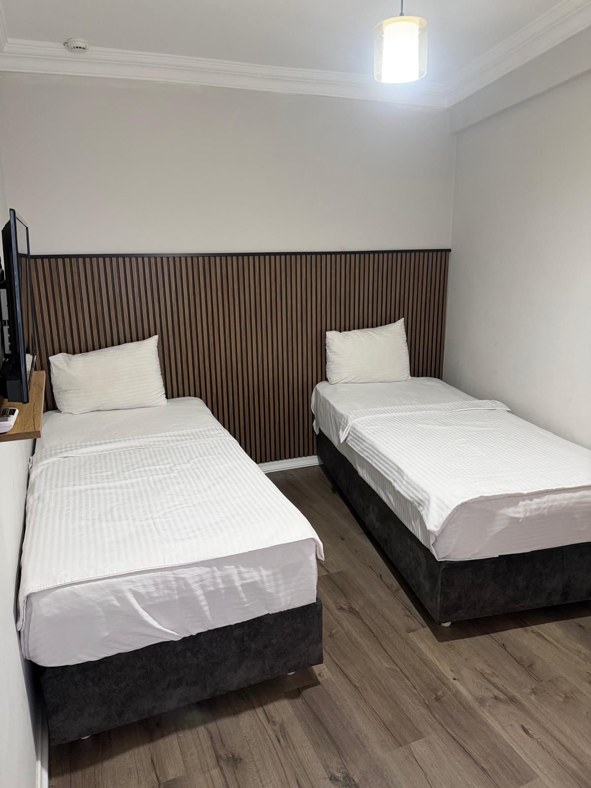 Hotellihuone, jossa on kaksi erillistä sänkyä, puinen pääty, taulutelevisio ja puulattia.