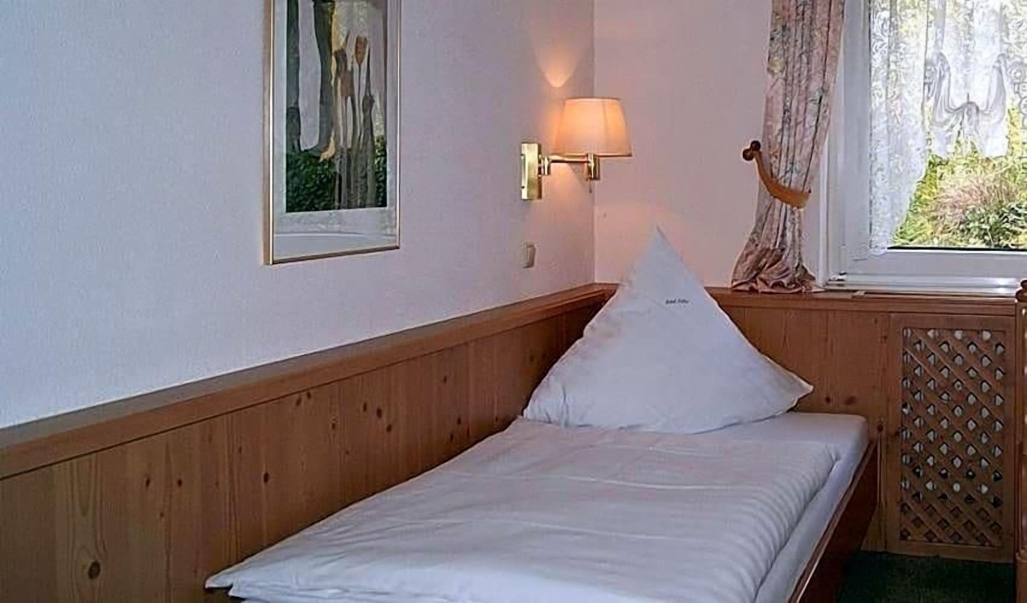 Ein Einzelbett mit Holzvorhang, eine Wandleuchte, ein gerahmtes Bild und ein Fenster mit Vorhängen.