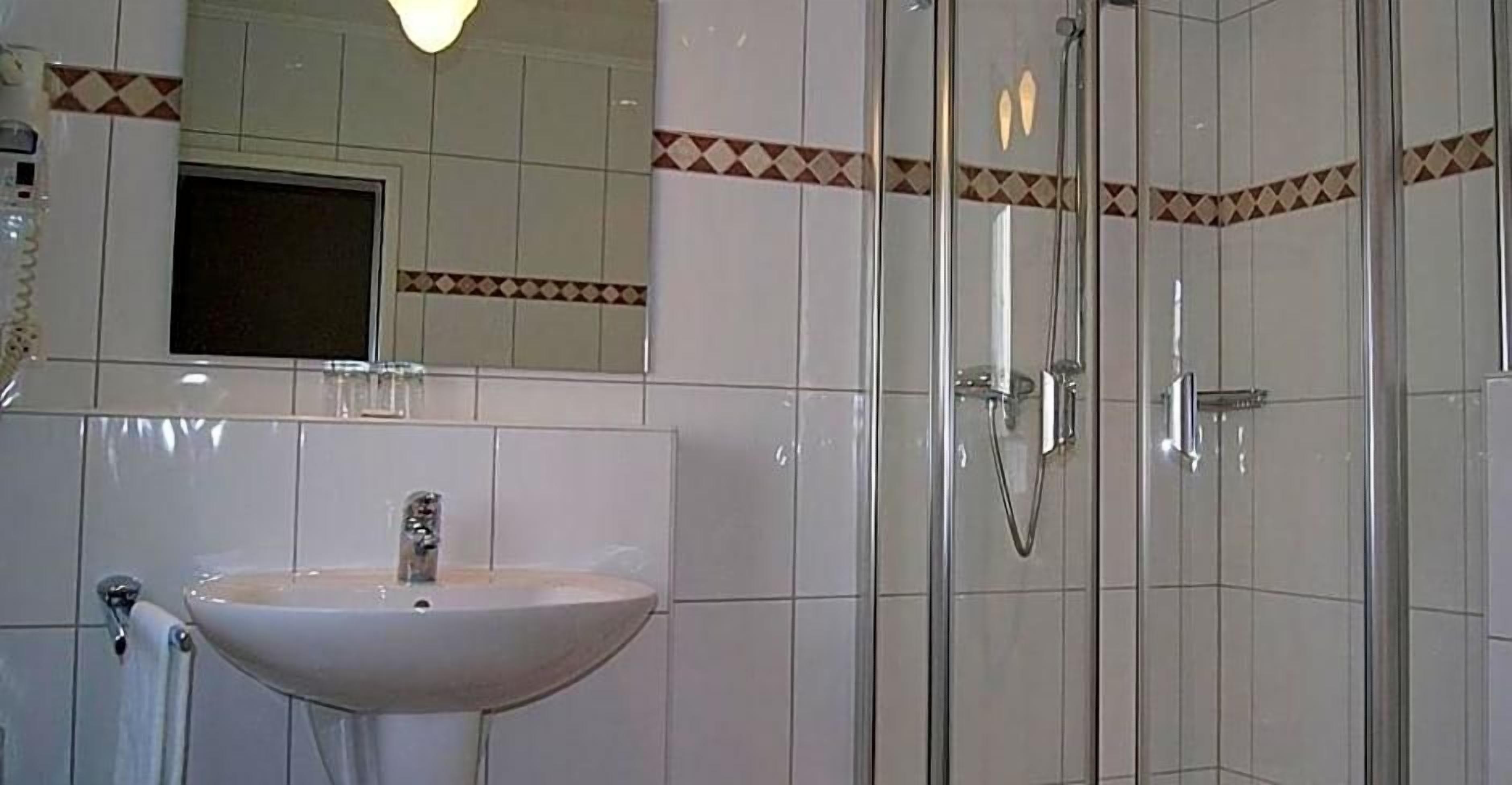 Ein Badezimmer mit Waschbecken, Spiegel, Dusche und Fliesenwänden.
