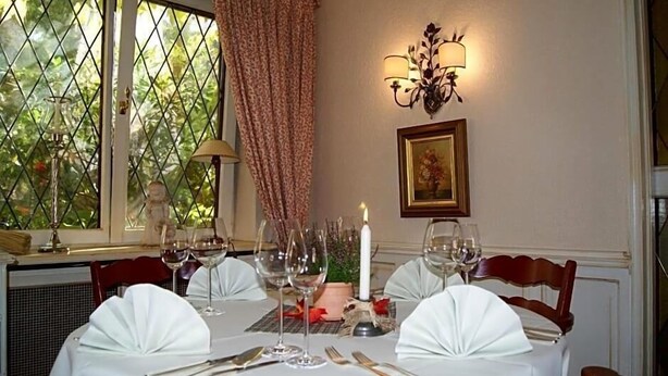 Mesa de comedor para seis personas, con mantel blanco, velas y copas de vino.