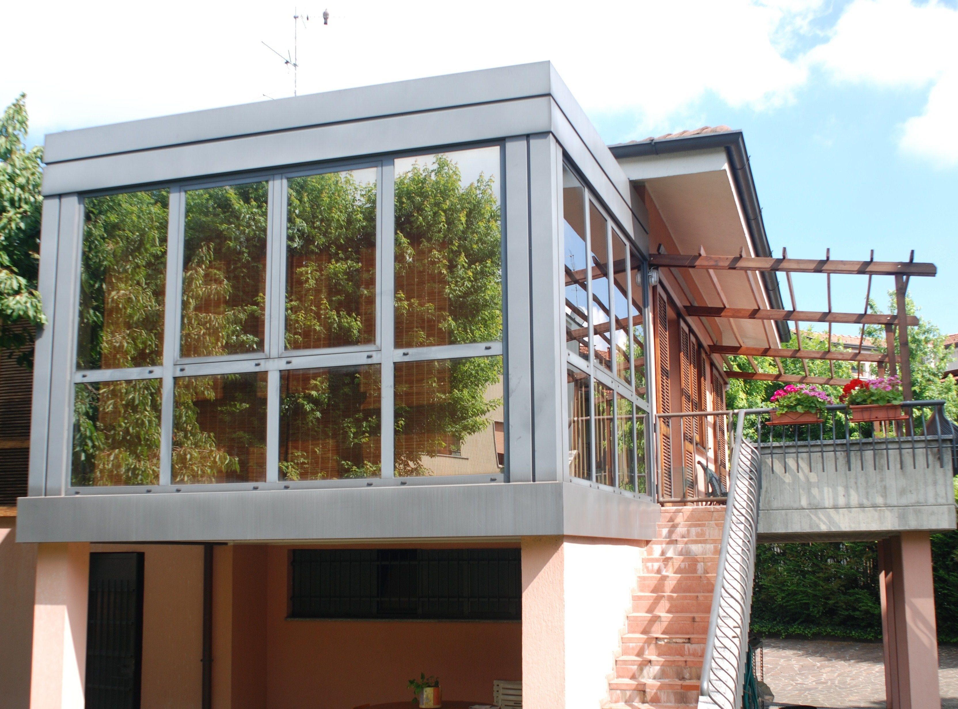 Ein modernes Gebäude mit großen Fenstern, einem Balkon mit einer Holz-Pergola und einer Treppe zum Eingang.