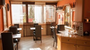 A restaurant with a tiled floor, wooden tables and chairs, a counter with a coffee machine, and a window with blinds. - Hotel Erzhausener Hof (Erzhausen)