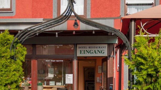 A hotel entrance with a red facade, a sign reading "HOTEL RESTAURANT EINGANG", and a pathway leading to the entrance. - Hotel Erzhausener Hof (Erzhausen)
