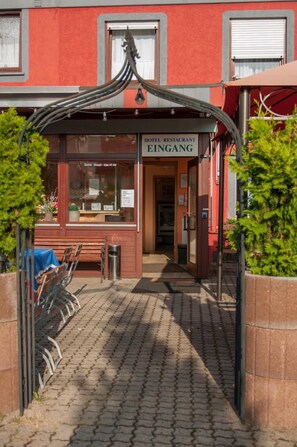 A hotel entrance with a red facade, a sign reading "HOTEL RESTAURANT EINGANG", and a pathway leading to the entrance. - Hotel Erzhausener Hof (Erzhausen)