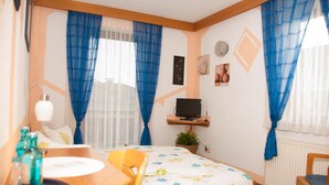 A hotel room with a bed, a desk with a chair, a TV on a shelf, and a window with blue curtains. - Hotel Erzhausener Hof (Erzhausen)