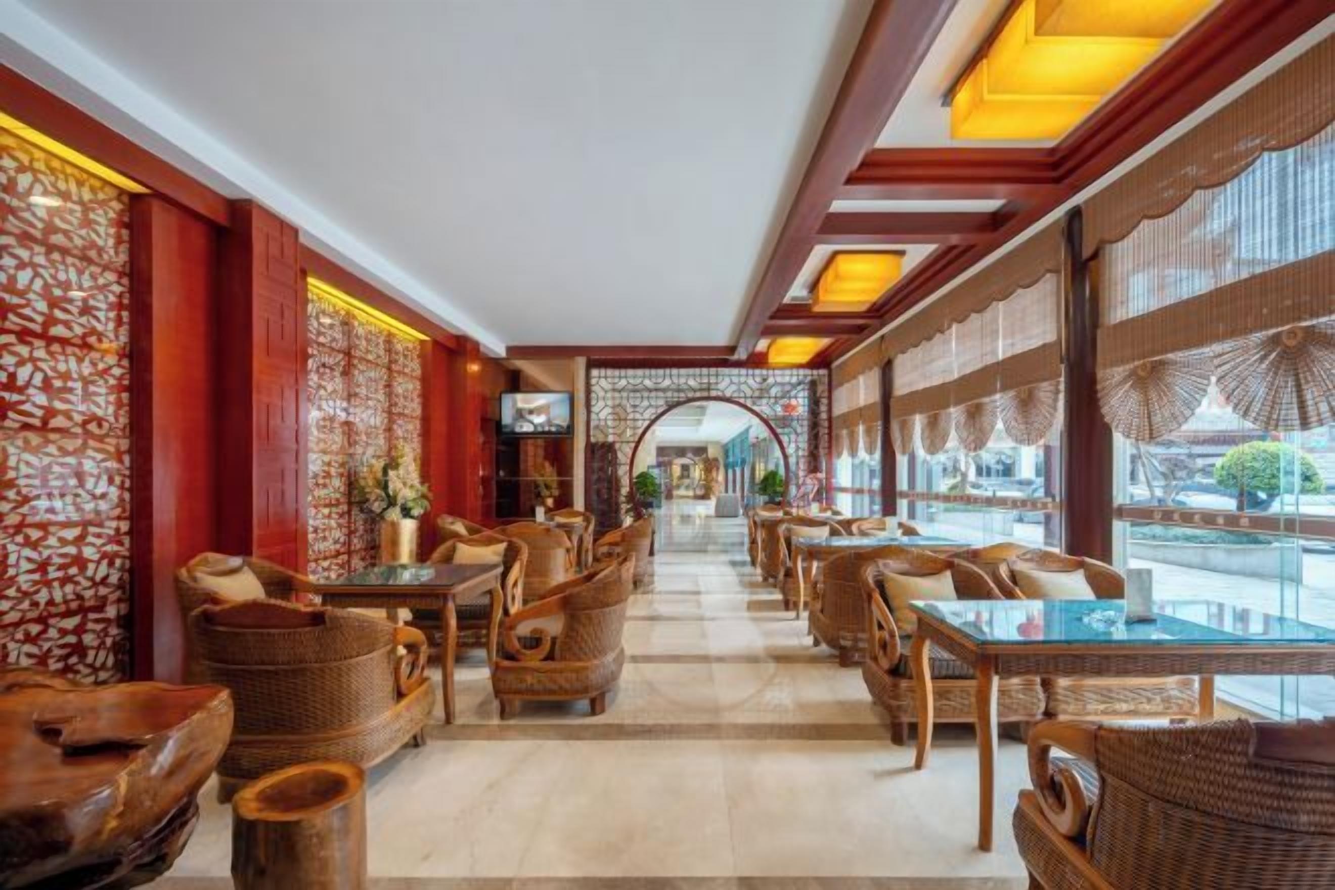 Un hall de hotel con mobiliario de mimbre, un arco central y vistas amplias a través de grandes ventanales.