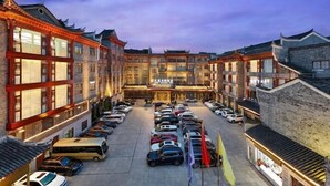 A hotel with traditional architecture, multiple floors, and a parking lot filled with cars. - Phoenix International Hotel (Fenghuang Ancient Town Branch) (Fenghuang County)