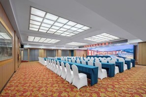 Ein Konferenzraum mit Tischen und Stühlen, einem Teppichboden und einem großen Bildschirm.