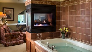 A living room with a fireplace, a large bathtub, and patterned furniture. - Lake Pointe Inn (McHenry)