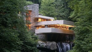A modern house with a stone facade, large windows, and a waterfall in the background. - Lake Pointe Inn (McHenry)