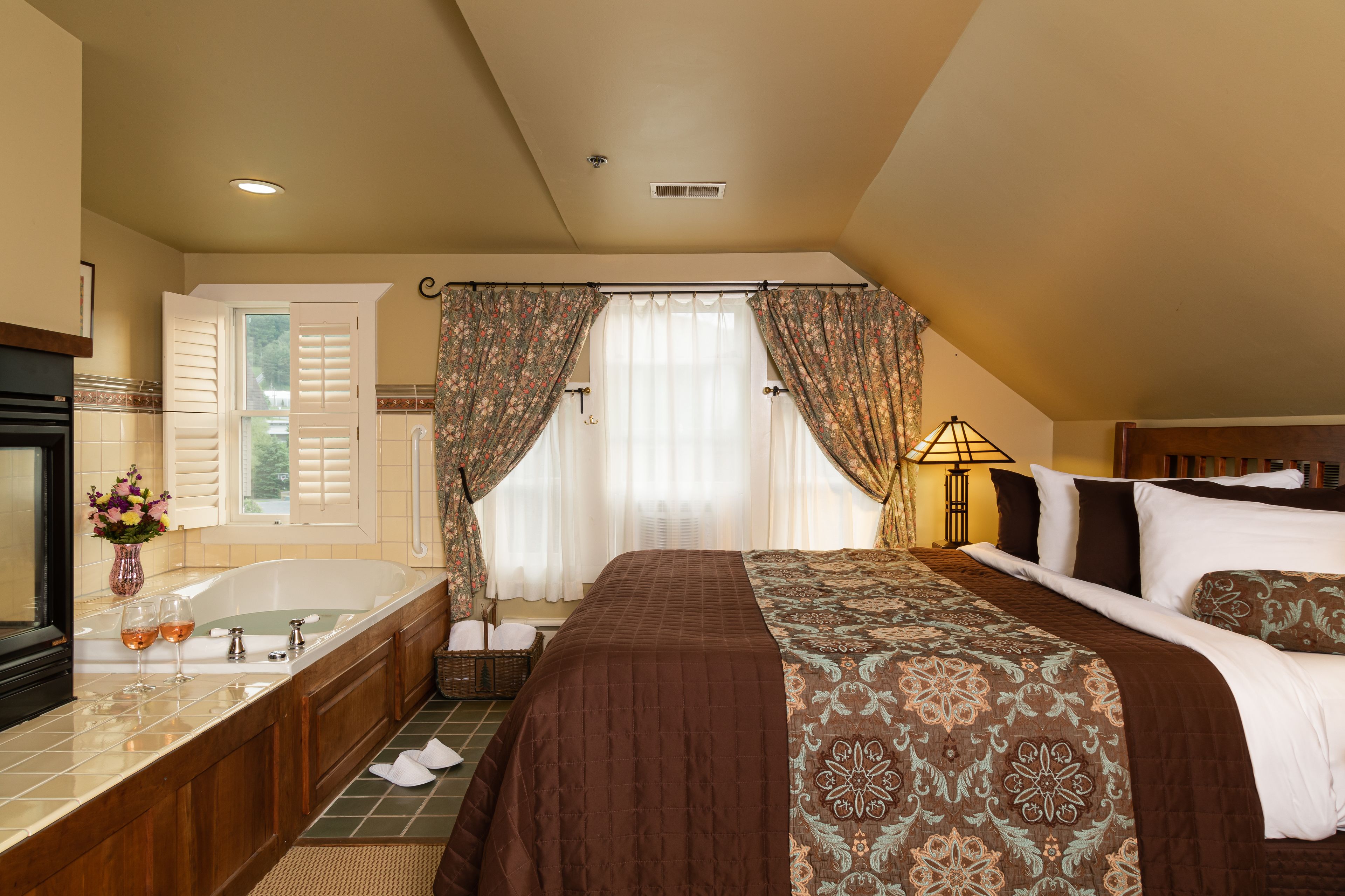 A hotel room with a large bed, a bathroom with a bathtub, and a window with curtains.