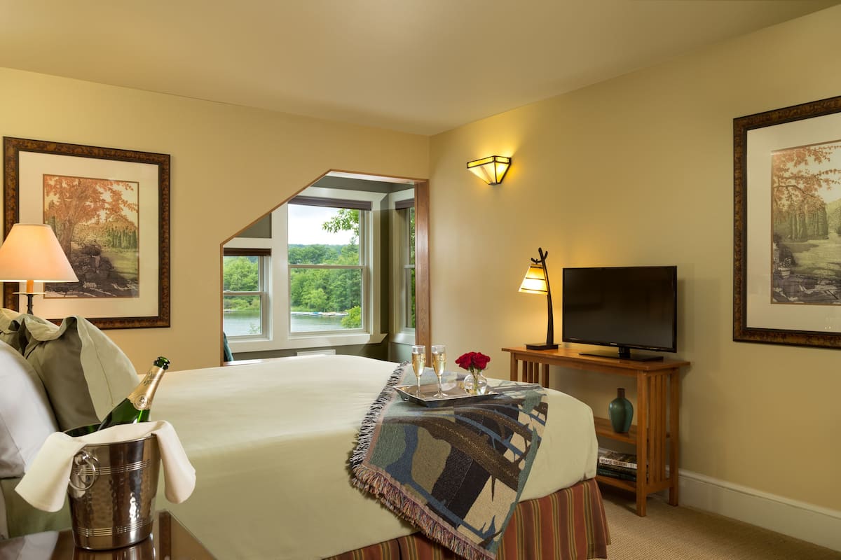A hotel room with a bed, a television, a window with a view of greenery, and a framed picture on the wall.