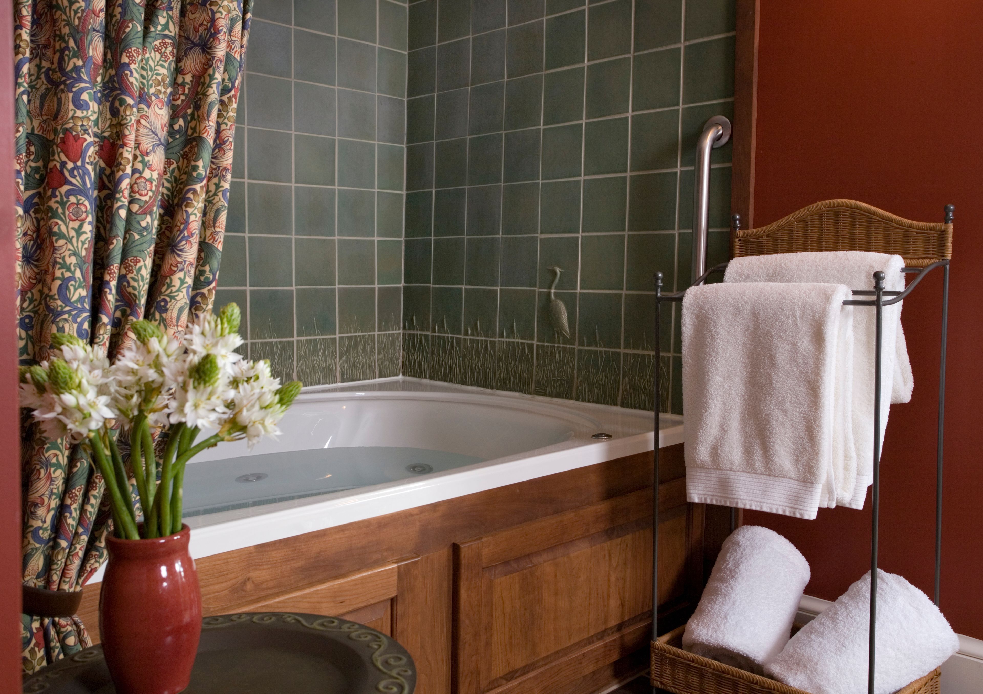 Une salle de bain avec une baignoire, une douche, un meuble en bois, un panier en osier contenant des serviettes et un vase avec des fleurs.
