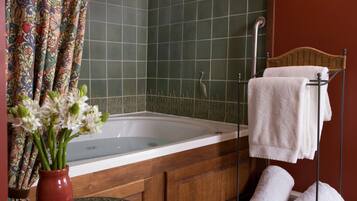 Une salle de bain avec une baignoire, une douche, un meuble en bois, un panier en osier contenant des serviettes et un vase avec des fleurs.