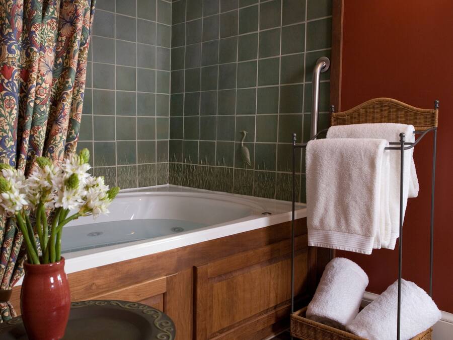 Une salle de bain avec une baignoire, une douche, un meuble en bois, un panier en osier contenant des serviettes et un vase avec des fleurs.