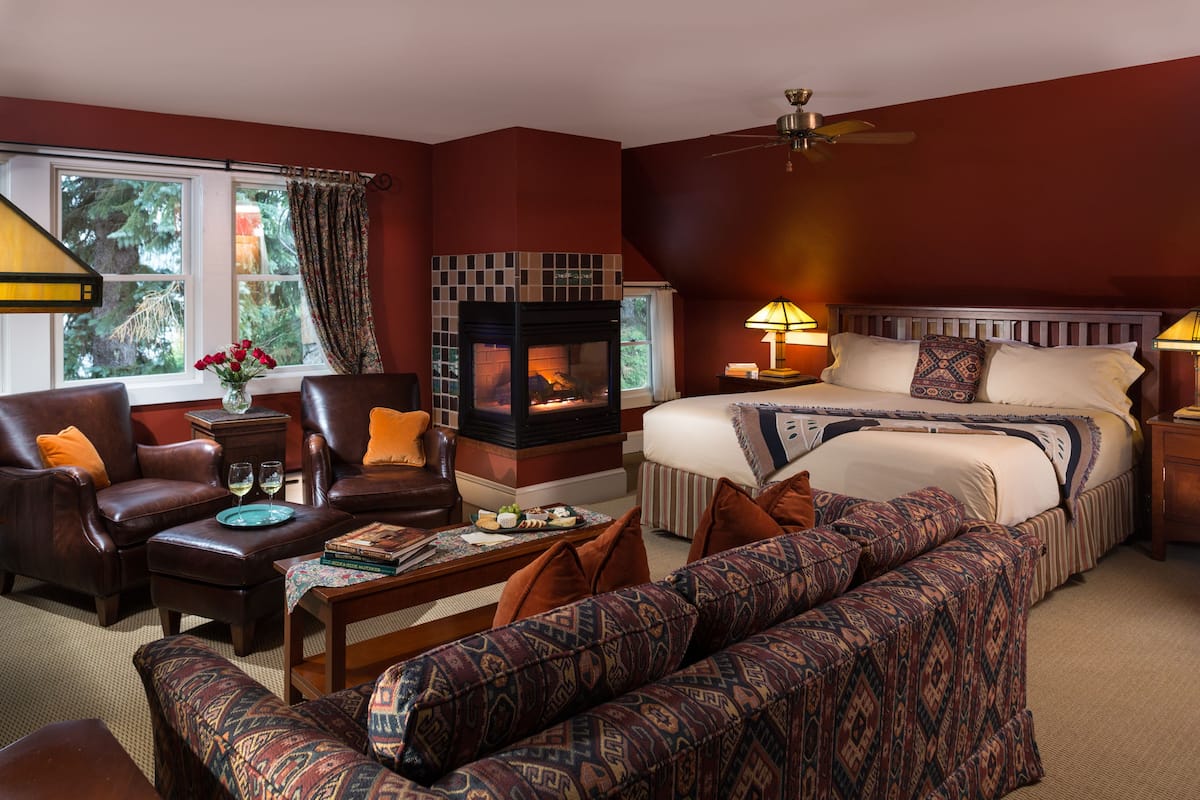A hotel room with a fireplace, a large bed, a sofa, a chair, and a dining table.