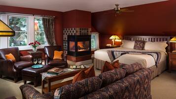 A hotel room with a fireplace, a large bed, a sofa, a chair, and a dining table.