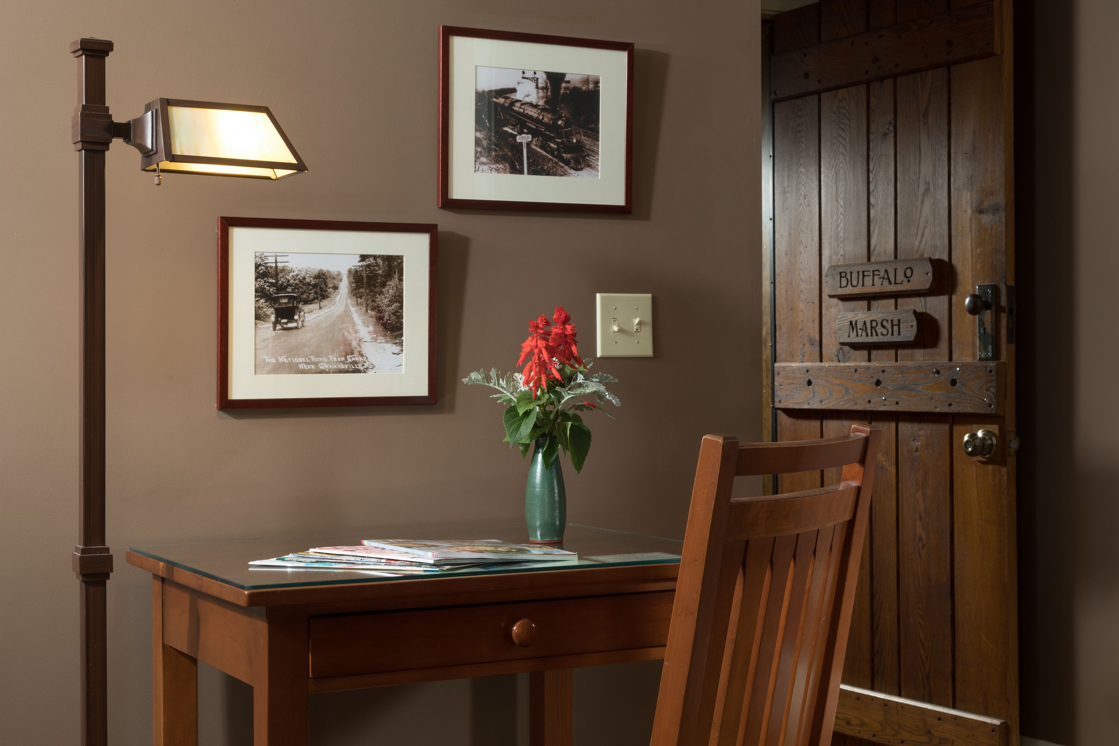 A wooden desk with a vase of flowers, framed pictures on the wall, and a door with a sign.