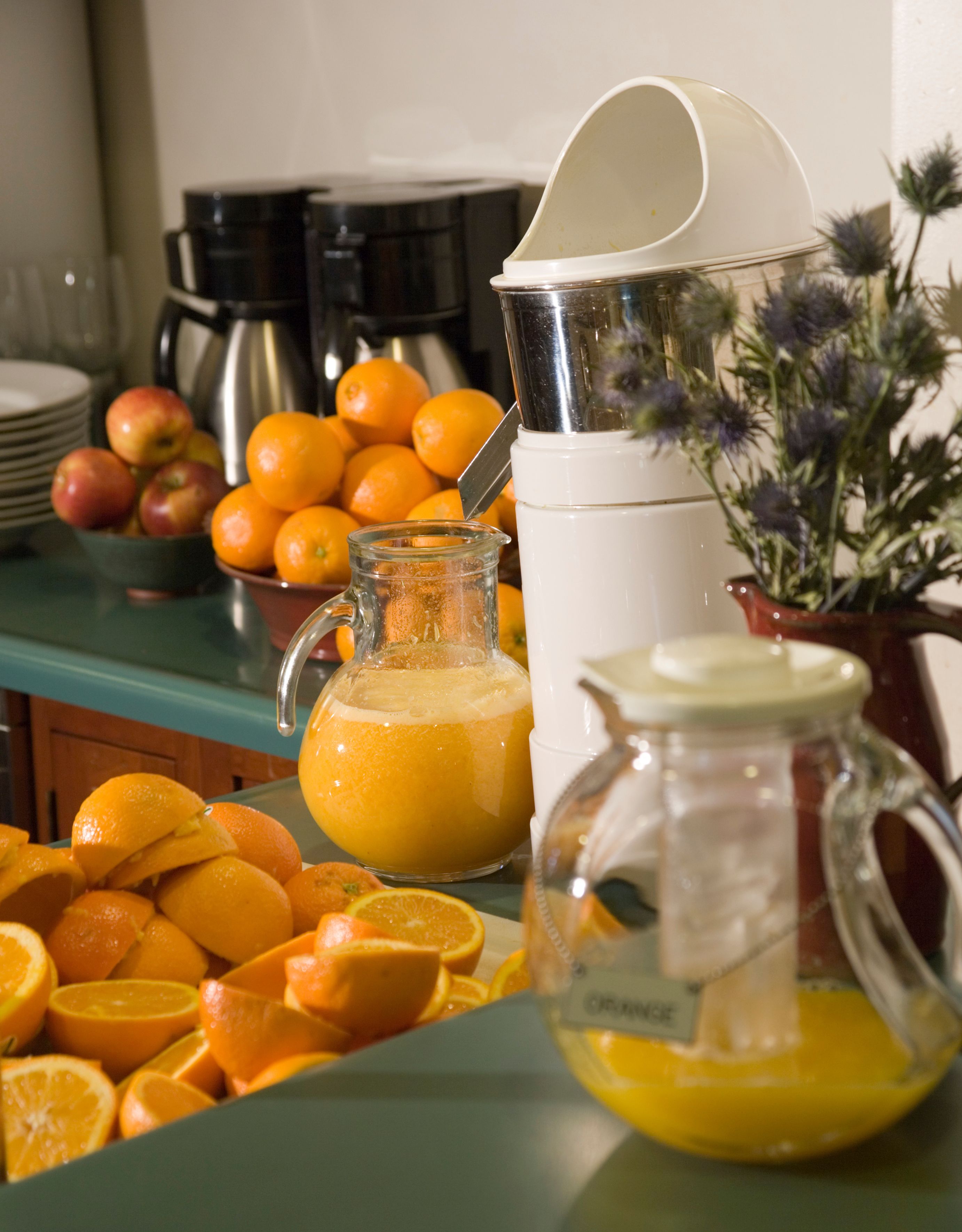 A breakfast buffet with oranges, a pitcher of orange juice, and a coffee maker.